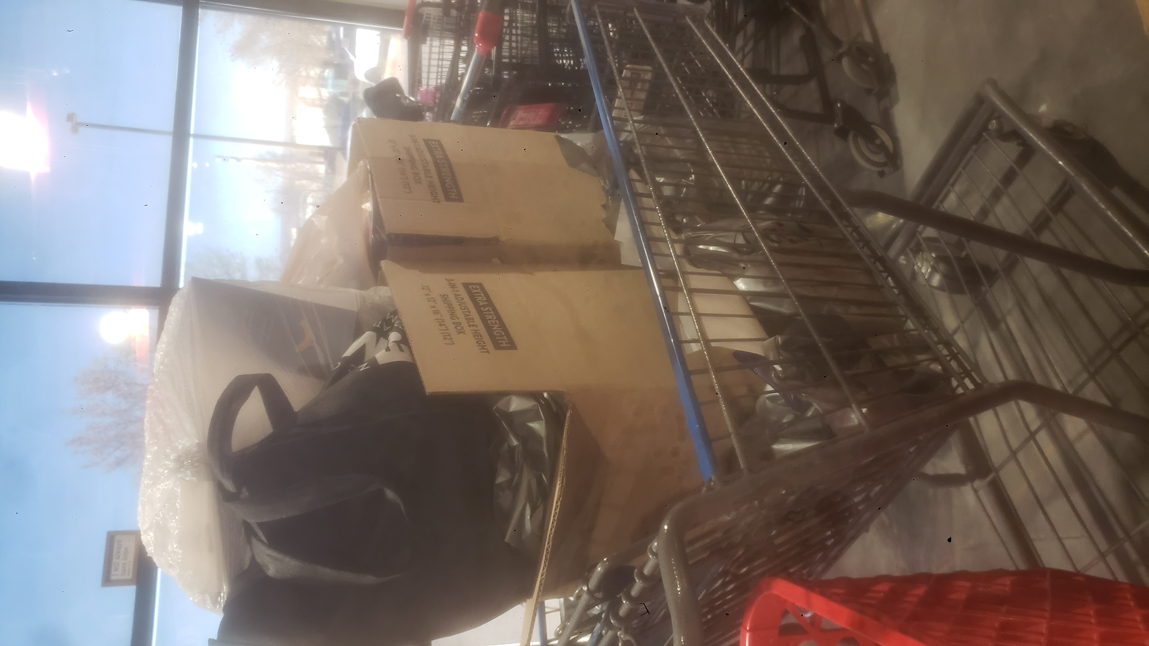 Shopping cart full of plastic bags and two cardboard boxes.